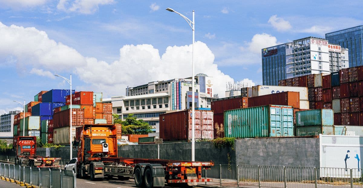 Tumpukan kontainer dan truk trailer di area bongkar muat pelabuhan.