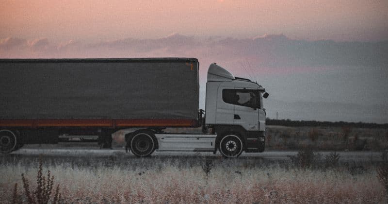 Truk trailer cargo melaju di jalan antar kota saat senja.