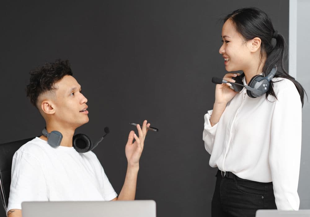 Dua staf layanan pelanggan mengenakan headset sedang berbincang.